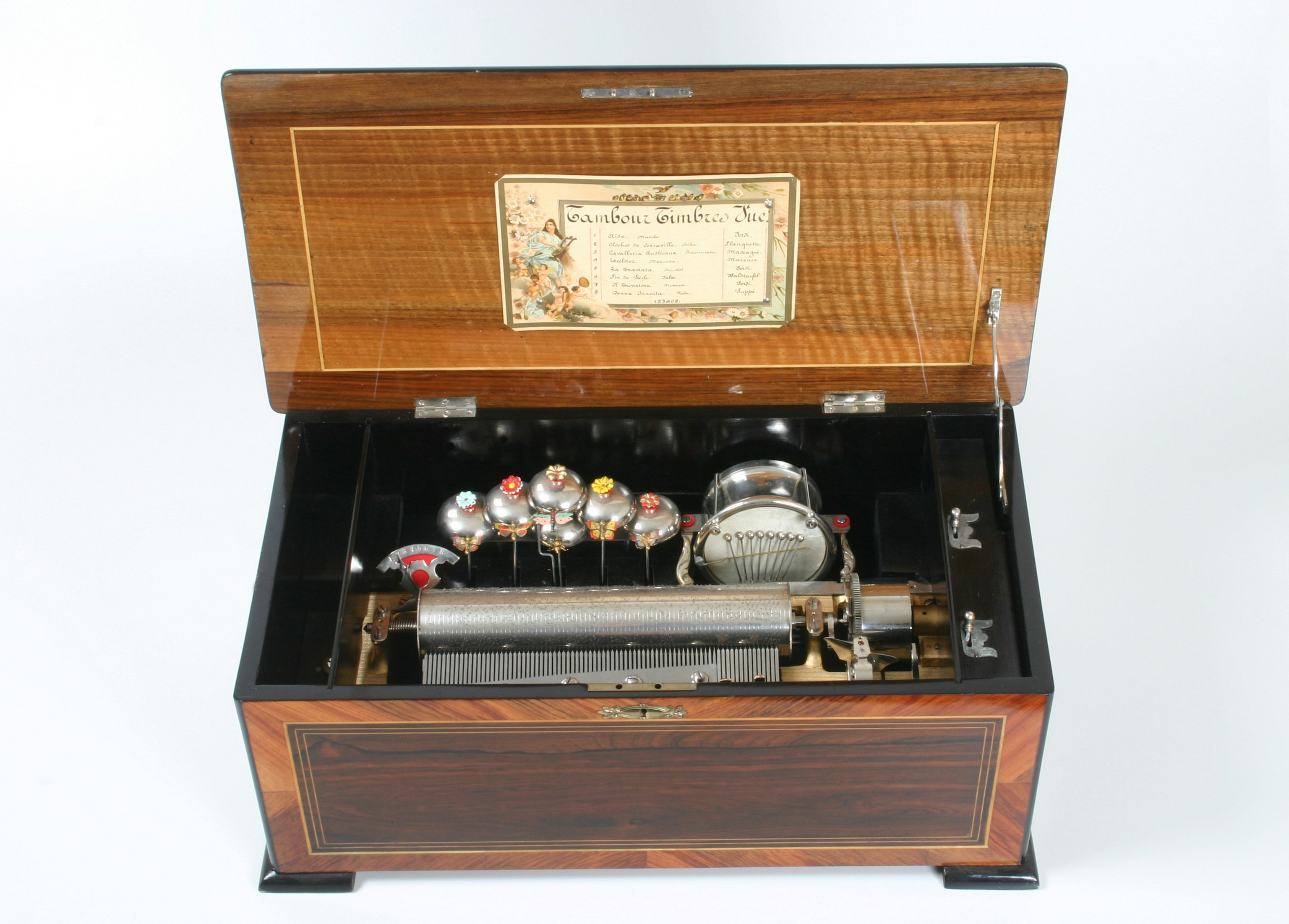 8 Musikstücke; Stimmkamm mit 66 Tönen; 6 Glocken und Trommel mit 8 Schlegeln. Das «Columbia»-Musikwerk wurde komplett von der Fa. Paillard & Cie., Ste-Croix, zugeliefert. 70 x 36 x 26 (56) cm (L. x T. x H., ( ) H. mit geöffnetem Deckel).